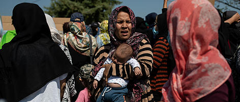 A woman holds a baby as refugees and migrants from the destroyed Moria camp protest near a new temporary camp, on the island of Lesbos